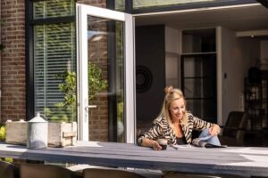 Vrouw aan tafel bij openslaande kunststof tuindeuren met veel lichtinval