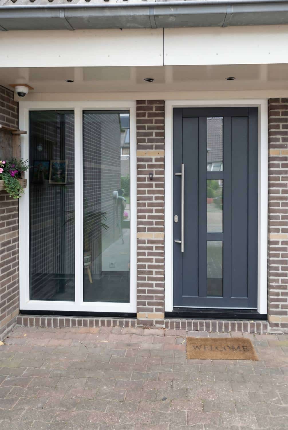 Moderne kunststof voordeur in RAL 7016 met wit zijlicht en welkomstmat, project Markant Kozijnen Hoogeveen.